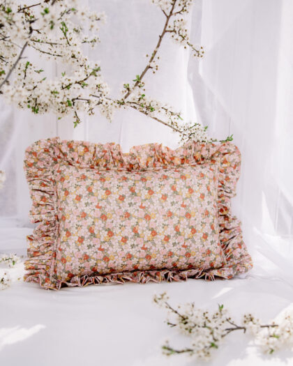 Poduszka ozdobna w drobne kwiaty z falbanami na tle białej tkaniny i kwitnące gałązki