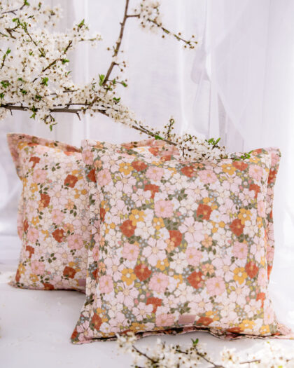 Dwie poduszki w kolorowe kwiaty na jasnym tle z gałązkami białych kwiatów w delikatnym świetle