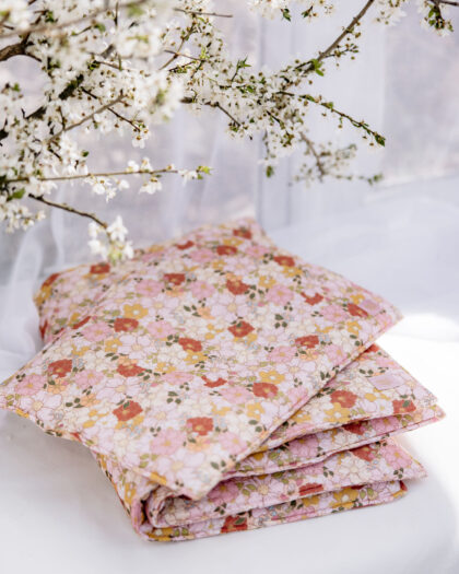 Złożona narzuta w pastelowe kwiatowe wzory na białym tle, z gałązkami białych kwiatów w tle