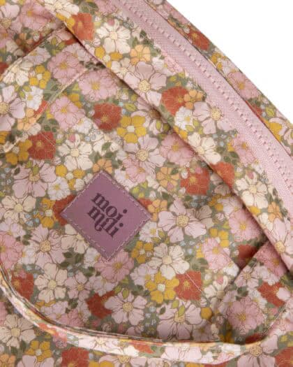 Detale różowego plecaka w kwiatowy wzór z małymi żółtymi, białymi i czerwonymi kwiatami oraz etykietą z napisem "moi nuli" na przedniej kieszeni.