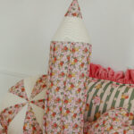 Miękka poduszka w kształcie ołówka w kwiatowy wzór na tle innych wzorzystych poduszek i pościeli.