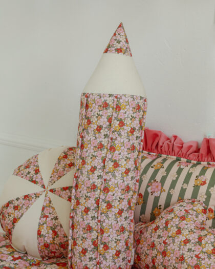 Miękka poduszka w kształcie ołówka w kwiatowy wzór na tle innych wzorzystych poduszek i pościeli.