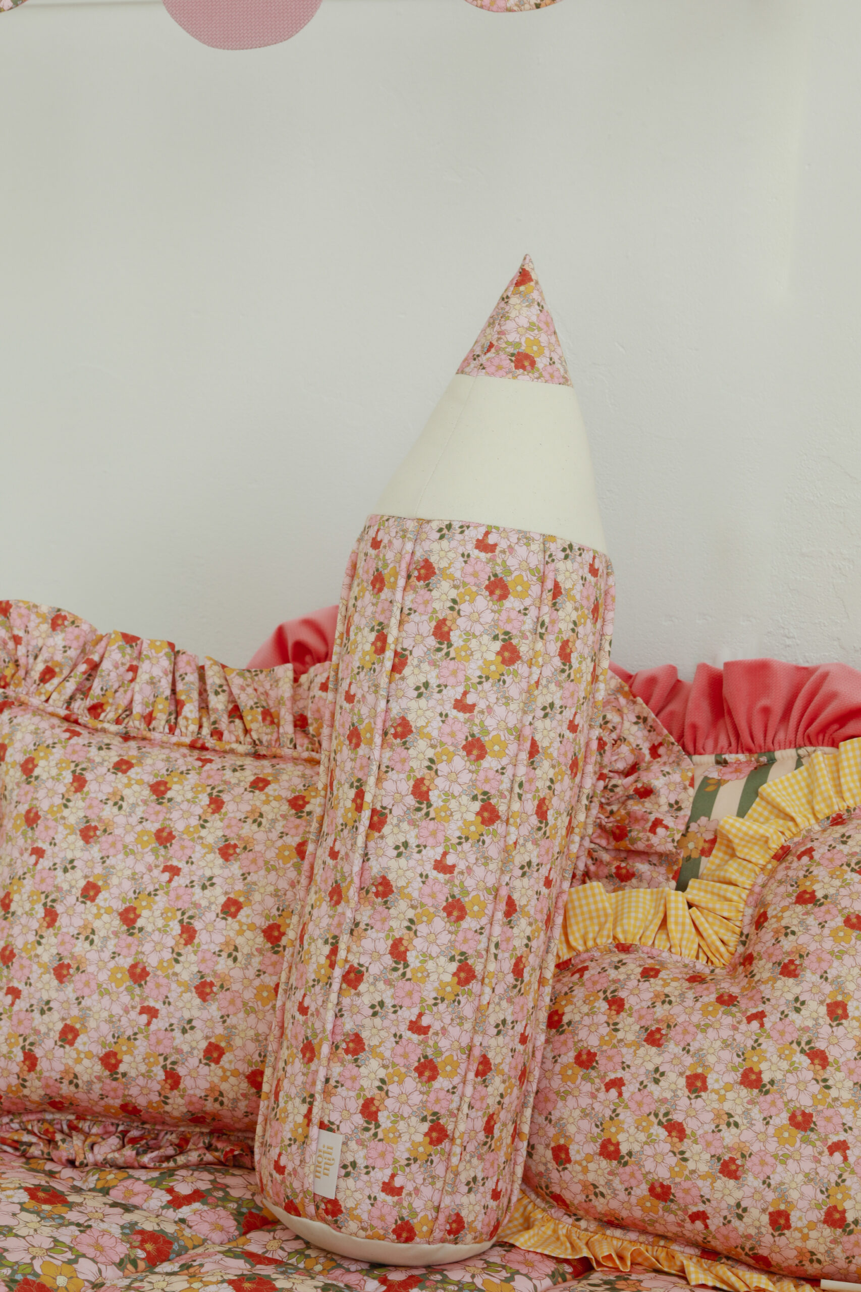 Poduszki z falbanami i wzorem kwiatowym w odcieniach różu oraz długa poduszka w kształcie ołówka