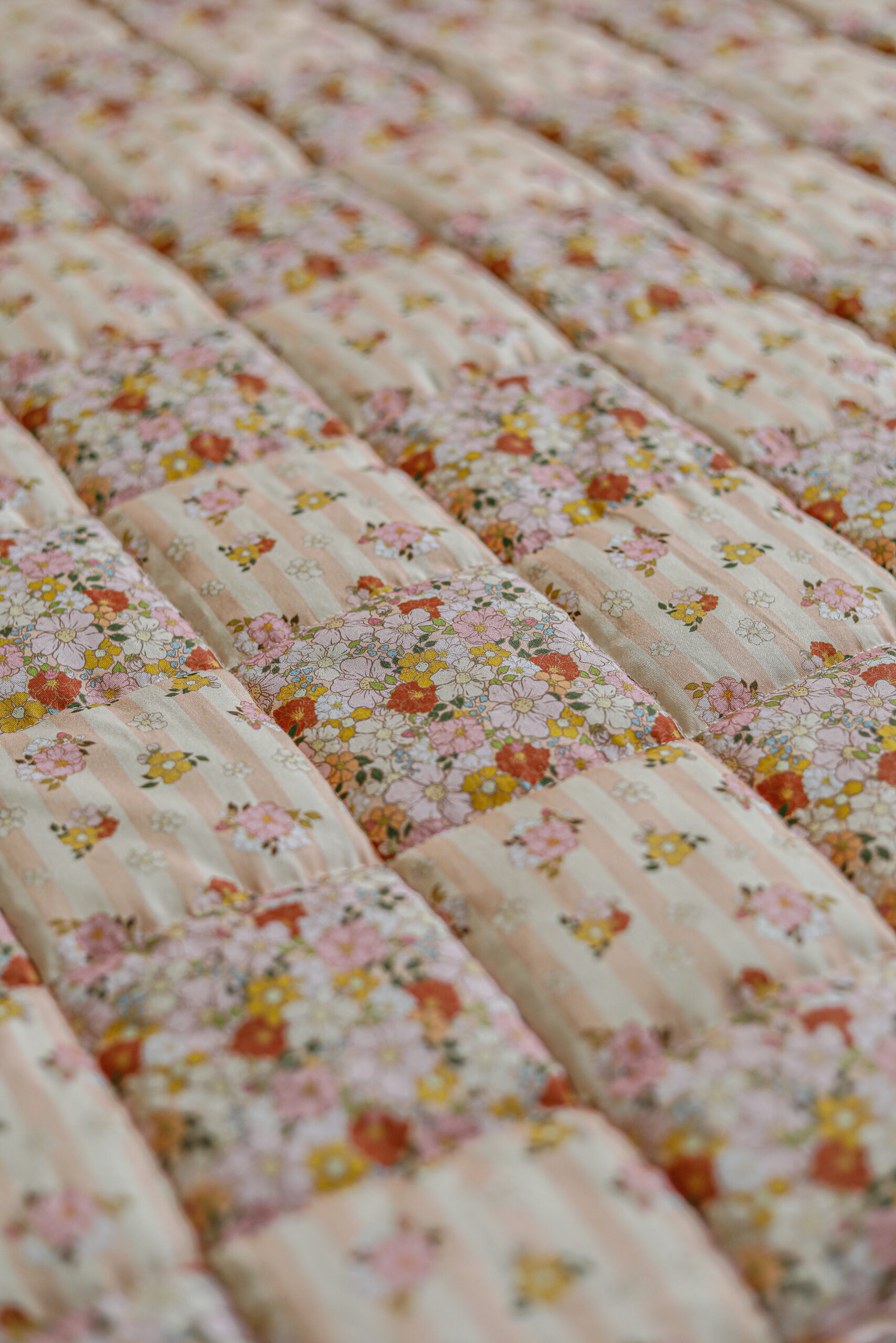 Zbliżenie na pikowaną narzutę w jasne pasy i kwiatowe wzory w pastelowych kolorach