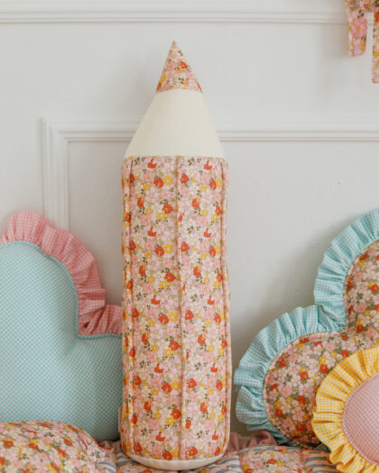 Poduszka w kształcie ołówka z kwiatowym wzorem wśród innych kolorowych poduszek na łóżku dziecięcym