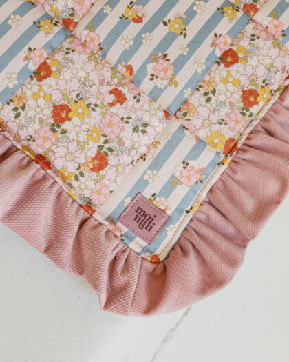 Kocyk dziecięcy z wzorem kwiatowym i paskami oraz różowym falbankowym obszyciem na jasnym tle