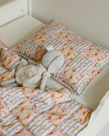 Bawełniana pościel w pastelowe kwiaty i paski oraz pluszowa szara zabawka na łóżku dziecięcym
