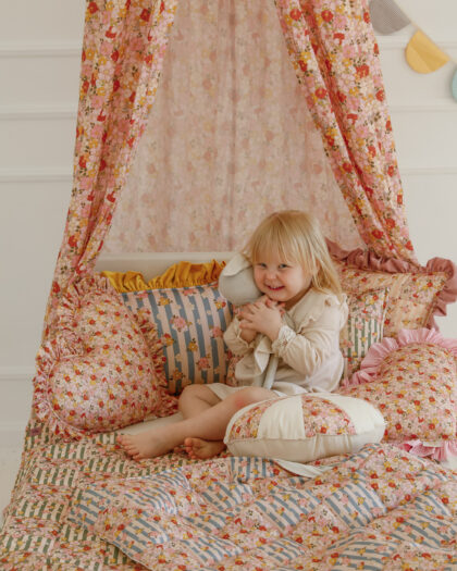 Mała dziewczynka bawi się na łóżku z kwiatowym baldachimem i kolorowymi poduszkami w pokoju dziecięcym