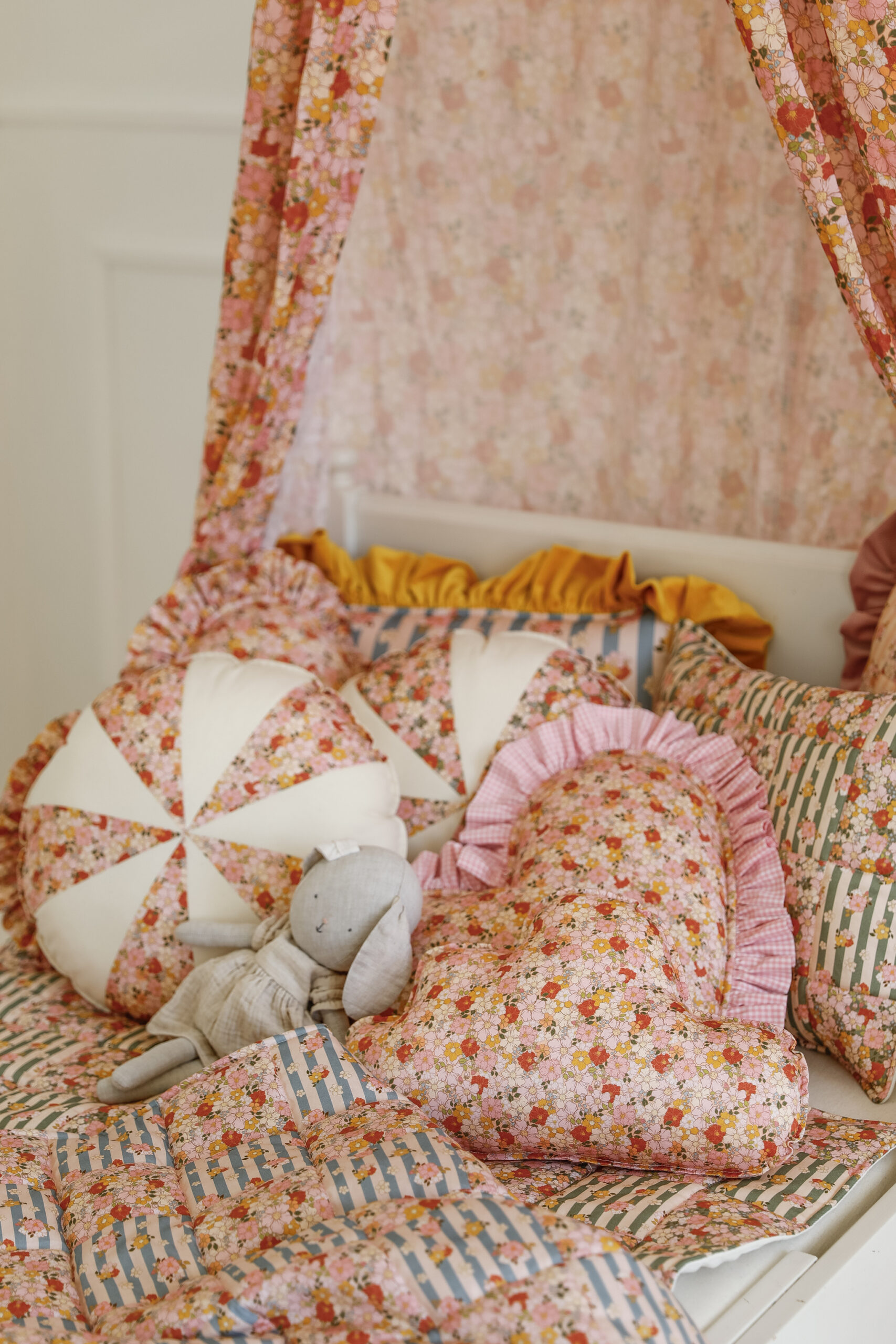 Przytulne łóżko dziecięce ozdobione różnymi poduszkami w kwiatowe wzory i pluszową zabawką królika
