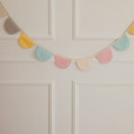 Kolorowa girlanda z tkanin w kratkę zawieszona na ścianie z białym zdobionym panelem