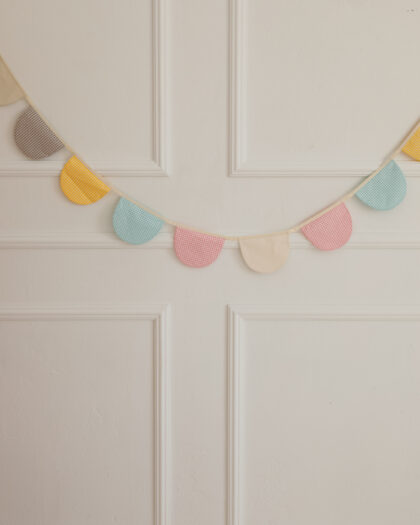 Kolorowa girlanda z tkanin w kratkę zawieszona na ścianie z białym zdobionym panelem