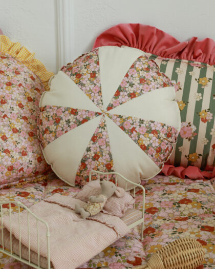 Małe białe łóżko z pościelą w różową kratę i pluszową myszką na kwiatowym i kolorowym tle poduszek