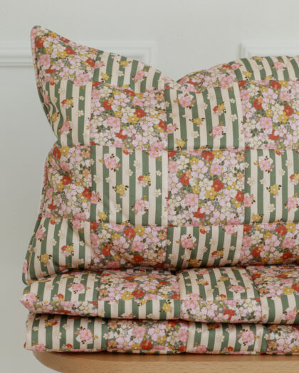 Składana pościel w kwiatowy wzór na zielono-beżowym tle, ułożona na drewnianym stołku w jasnym pomieszczeniu