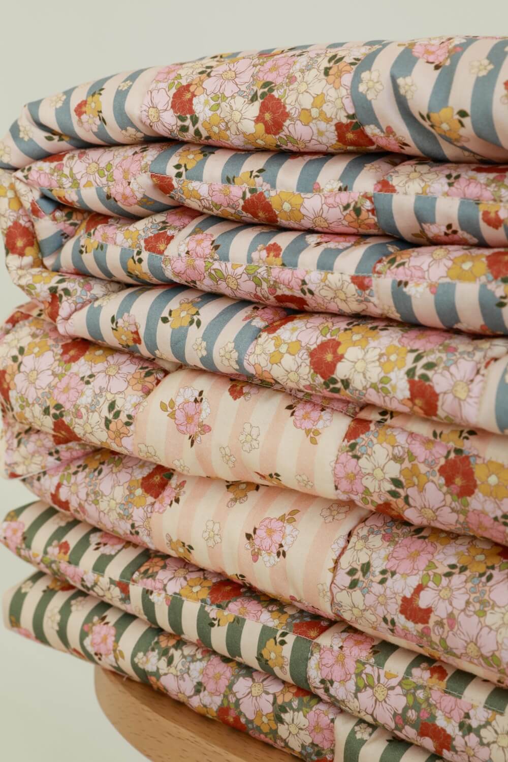 Stos złożonych tkanin w pastelowe paski z kolorowymi kwiatowymi wzorami ułożonych na drewnianym stojaku