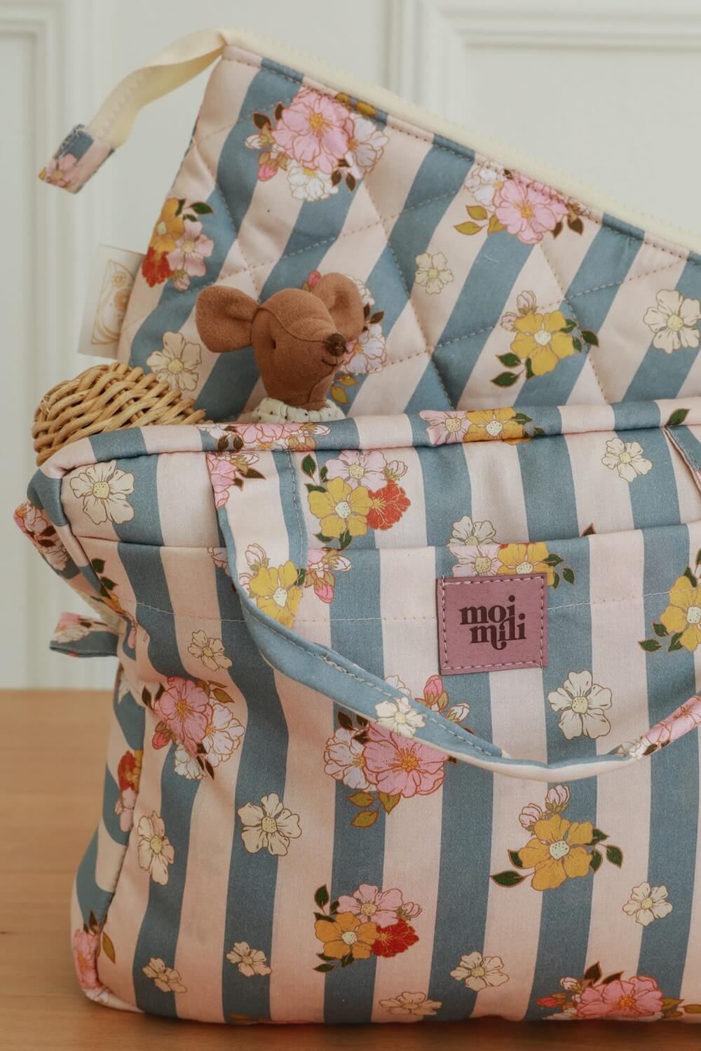 Torba w pastelowe paski i kwiaty z maskotką myszki i wiklinowym koszykiem na drewnianym stole