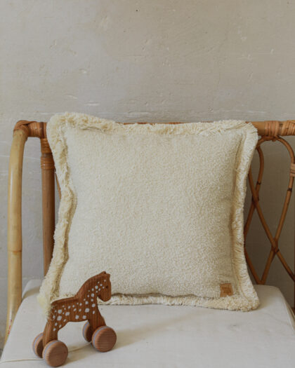 Jasna poduszka z frędzlami na wiklinowym fotelu i drewniana zabawka konik na kółkach