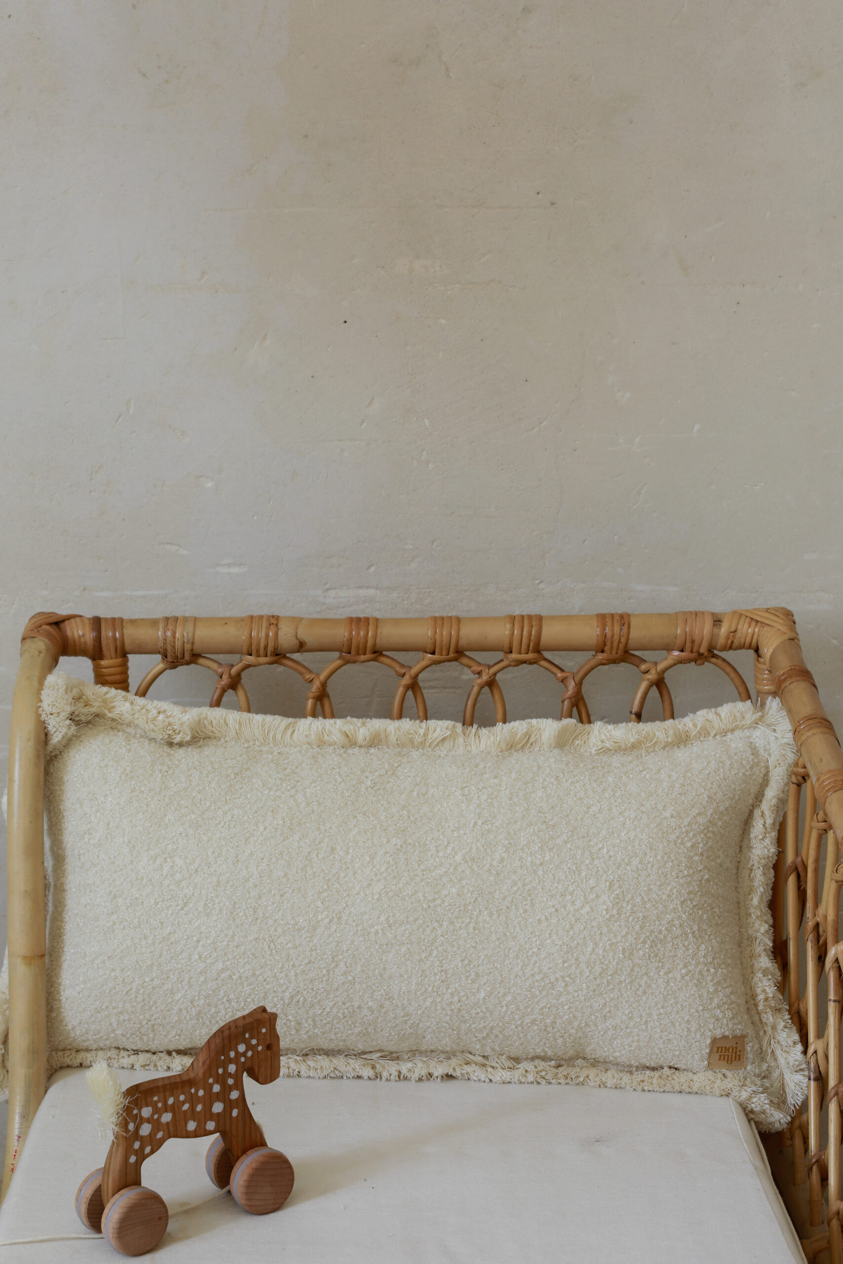 Naturalna poduszka dekoracyjna na wiklinowej sofie obok drewnianej zabawki w kształcie konika na kółkach