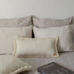 Beżowe poduszki na łóżku w neutralnych odcieniach i czarna książka Kinfolk na pościeli