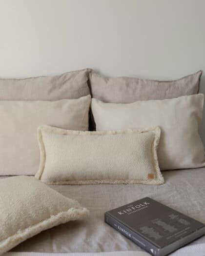 Beżowe poduszki na łóżku w neutralnych odcieniach i czarna książka Kinfolk na pościeli