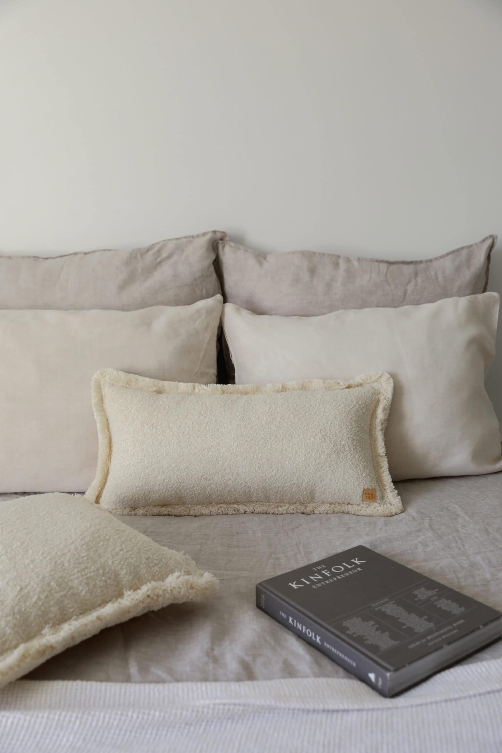 Beżowe poduszki na łóżku w neutralnych odcieniach i czarna książka Kinfolk na pościeli