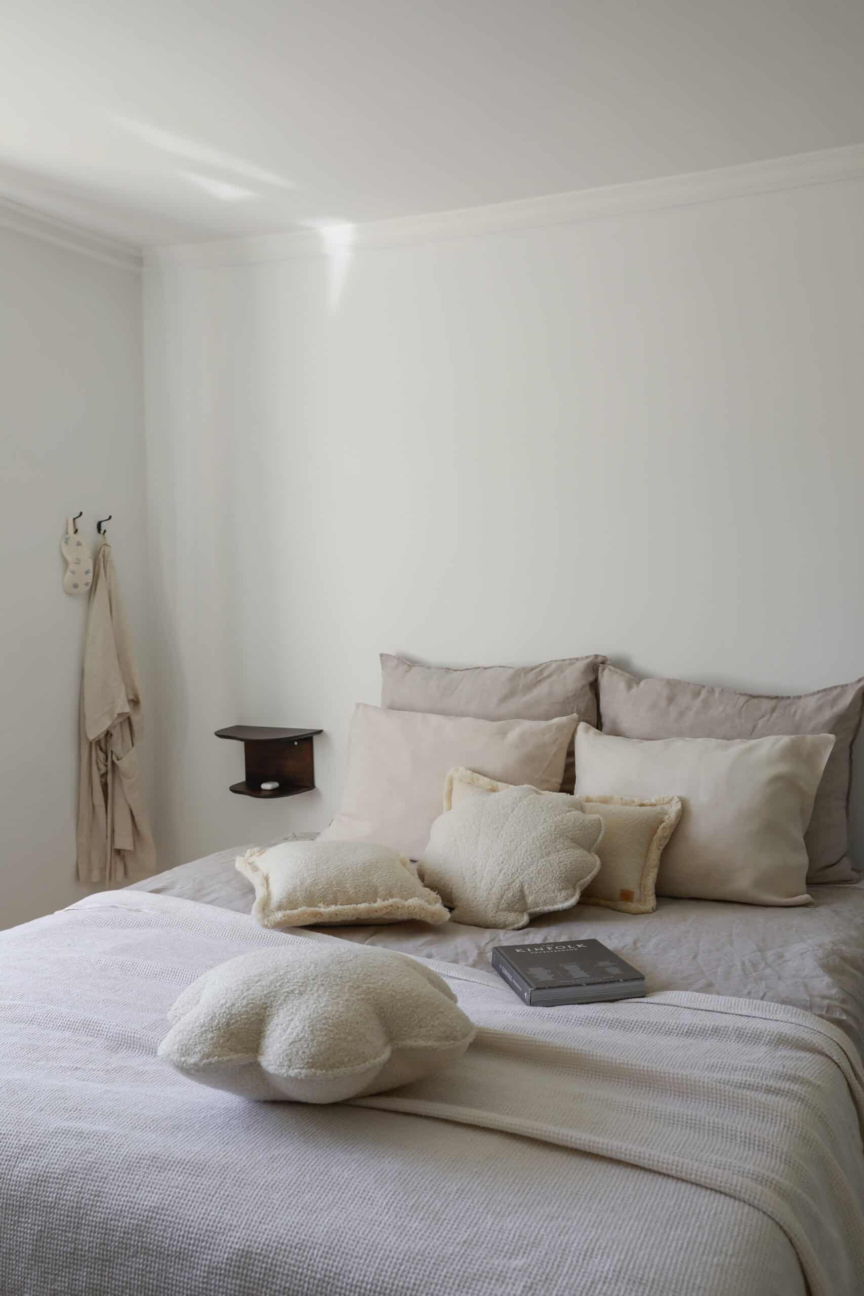 Przytulna sypialnia z beżowymi poduszkami i miękką narzutą na łóżku w jasnym wnętrzu.