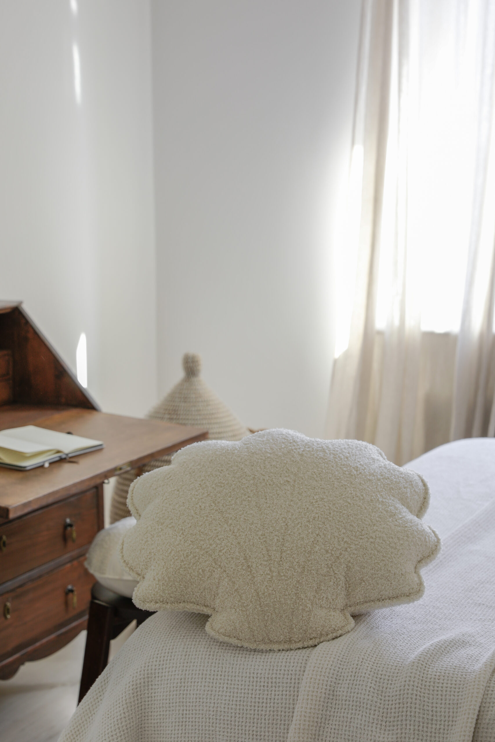 Poduszka w kształcie muszli na łóżku w jasnym pokoju z drewnianym biurkiem i otwartym zeszytem