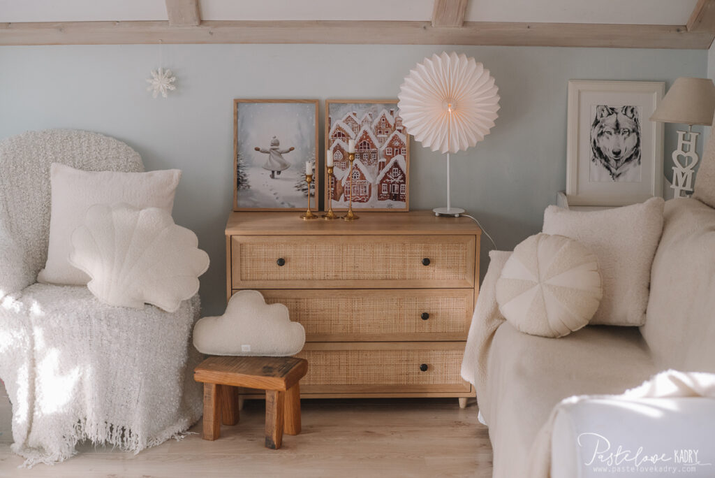 Przytulny pokój z jasnymi poduszkami, drewnianą komodą i dekoracyjnymi obrazami na ścianie