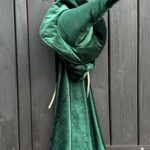 Zielony aksamitny kapelusz czarownicy z szerokim rondem i wysokim, zakrzywionym szpicem, wiszący na drewnianych deskach drzwi.
