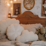 Przytulne łóżko dziecięce z drewnianym zagłówkiem, na którym leżą beżowe poduszki w kształcie obłoków i koła oraz pluszowy miś, a pomieszczenie zdobią obrazy ze Scooby-Doo, lisem oraz świętym Mikołajem z jelonkami i lampki w kształcie gwiazdy