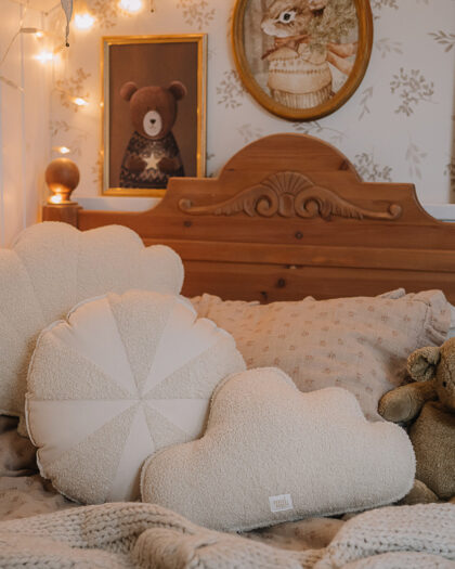 Przytulne łóżko dziecięce z drewnianym zagłówkiem, na którym leżą beżowe poduszki w kształcie obłoków i koła oraz pluszowy miś, a pomieszczenie zdobią obrazy ze Scooby-Doo, lisem oraz świętym Mikołajem z jelonkami i lampki w kształcie gwiazdy