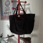 Czarna torba z długimi uchwytami zawieszona na czerwonym stojaku na ubrania, z rowerem w tle.